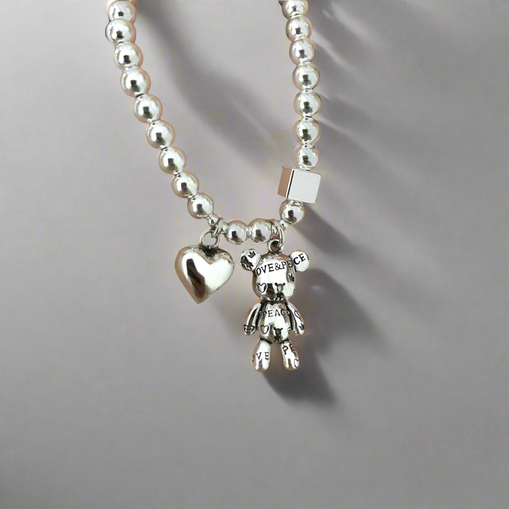 Front view of the Love & Peace Teddy Charm Bracelet in sterling silver with a teddy bear and heart-shaped pendant.